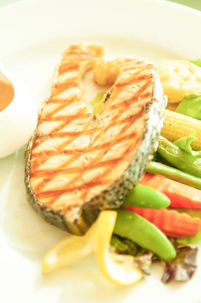 Grilled salmon with lemon and salad on white plate, blurred green background.