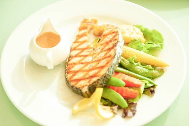 istock Grilled salmon with lemon and salad on white plate, blurred green background. 1133416741