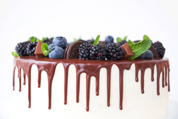 istock Cake with chocolate, decorated with backberries, blueberries, mint leaves, chocolate bars and cookies on a white table. 1133423181