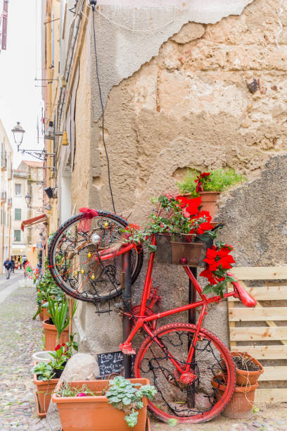 Alghero, Sardinia island, Italy - December 28, 2019: Colorful red bike with flowers in the street of Alghero, Sardinia island in Italy