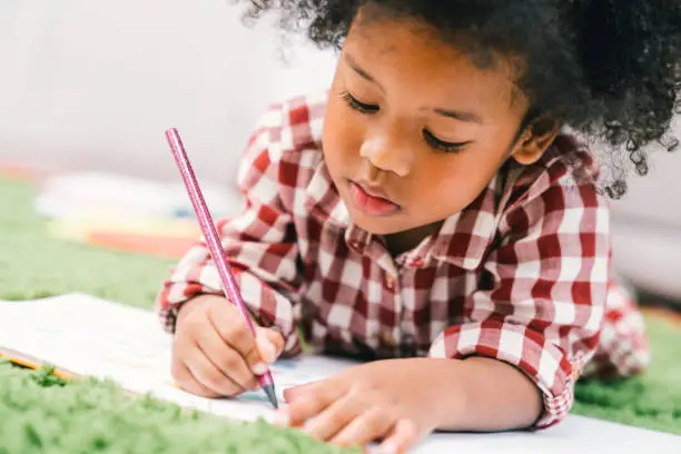 Cute young African American kid girl drawing or painting with colored pencil. Kindergarten children education, or preschool child study at home concept