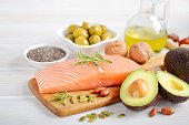 Selection of healthy unsaturated fats, omega 3 - fish, avocado, olives, nuts and seeds.