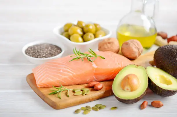 Selection of healthy unsaturated fats, omega 3 - fish, avocado, olives, nuts and seeds, selective focus.