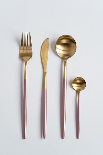 New luxury Golden cutlery view from above on a isolated white background. Top view. Pink knife, fork and spoon for a festive table for a wedding, birthday or party.