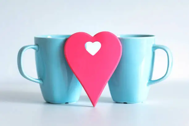 Red heart in front of two blue cups on white