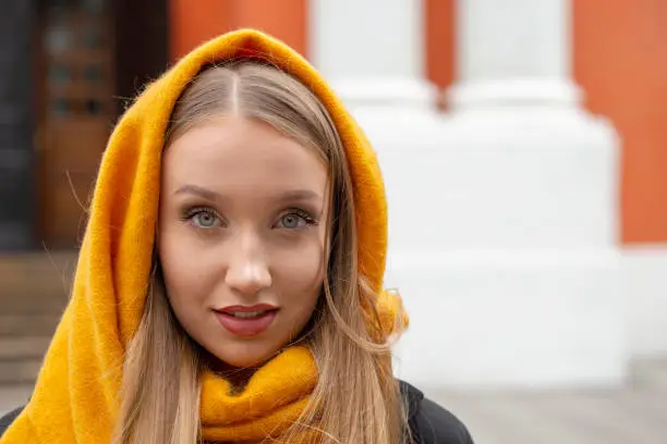 Autumn portrait of a blonde girl with long hair in a yellow scarf against the background of an ancient building with columns.