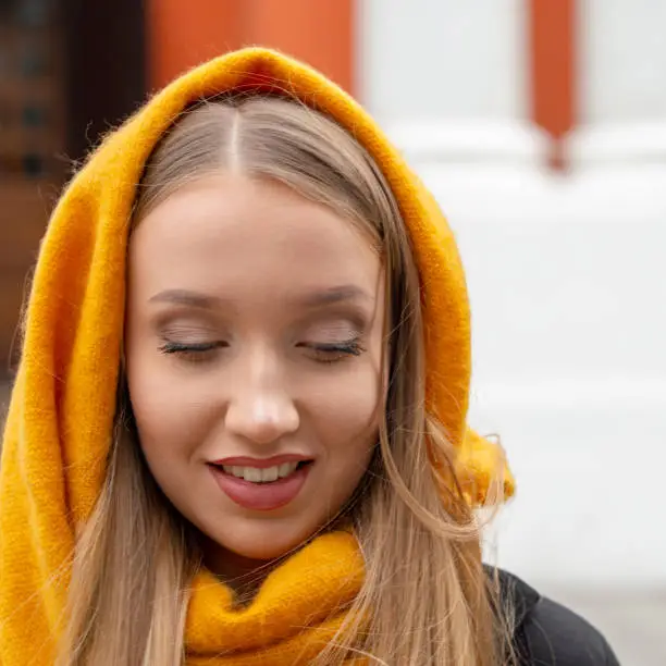 The girl in the yellow scarf is dreaming and smiling. Autumn portrait of a blonde with long hair.