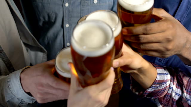 Friends clinking beer glasses, celebrating favorite sports team victory in pub