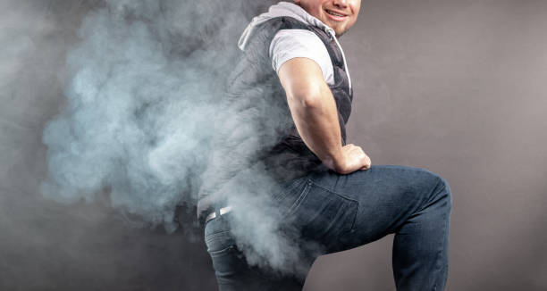 Man lift the leg and fart in front of grey background stock photo