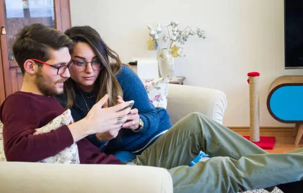 Young couple is looking carefully at smartphone on sofa in living room