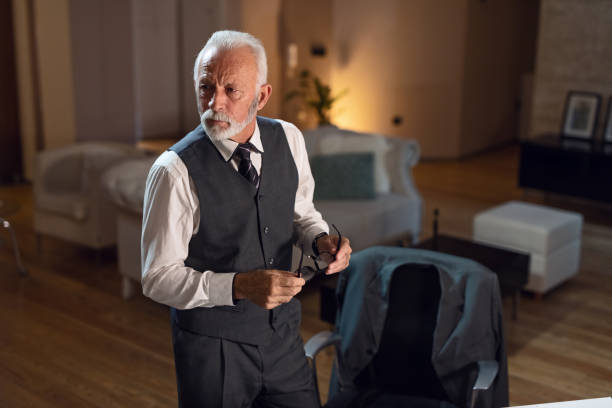 istock Serious senior businessman holding eyeglasses while standing at home office. 1133454412