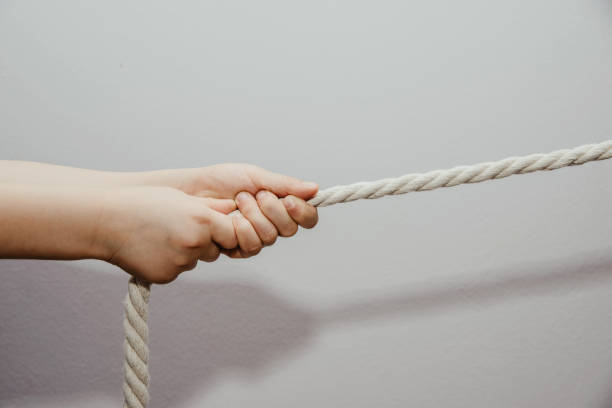 istock Dragging a rope by a child. The child struggles and pulls the rope on a bright gray background. 1133460062
