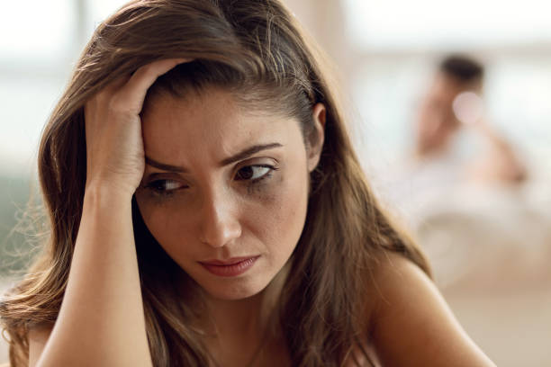 Young woman feeling depressed while having problems in her relationship. Close up portrait of sad young woman with smudged up mascara thinking about relationship problems. Her boyfriend is in the background. woman mascara smudged stock pictures, royalty-free photos & images
