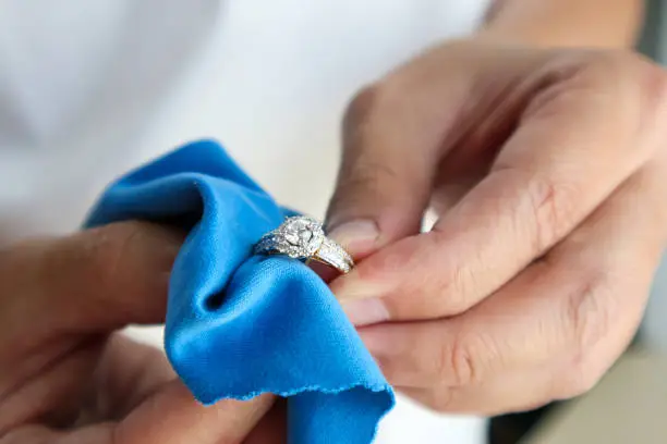 Photo of Jeweller hand polishing and cleaning jewelry diamond ring with micro fiber fabric