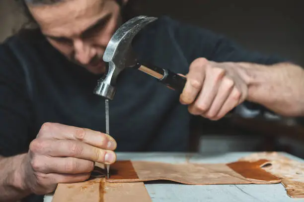 workshop of making the carved leather bag - craftsman punches edge of leather detail for handbag by stitching punch and hamme