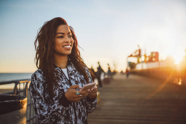 молодая модная женщина текстовых сообщений на свой телефон в санта-монике, la - long hair beauty adult attractive female стоковые фото и изображения