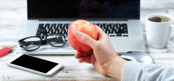 Male hand holding apple fruit with workstation technology in background Close of male hand holding fresh apple with workstation technology in background for business or education use wooden flash drive stock pictures, royalty-free photos & images