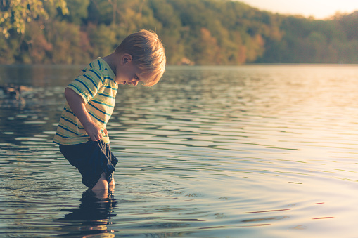 A young boy standing in a lake with the water up to his knees when suddenly he realizes his shorts are getting wet.