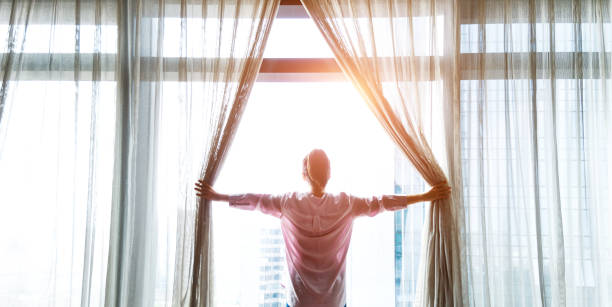 donna che apre tende e guarda fuori - waking up window women morning foto e immagini stock