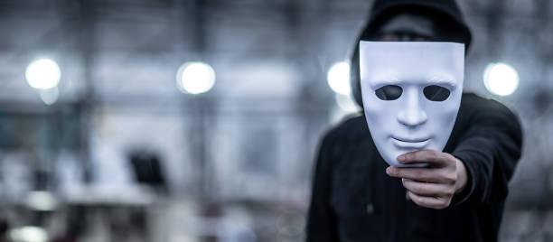 Mystery hoodie man with black mask holding white mask in his hand. Anonymous social masking or bipolar disorder concept. Mystery hoodie man with black mask holding white mask in his hand. Anonymous social masking or bipolar disorder concept. mask disguise stock pictures, royalty-free photos & images