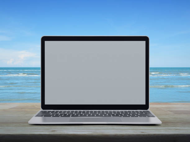 istock Modern laptop computer with blank grey screen on wooden table over tropical sea and blue sky with white clouds 1133506686