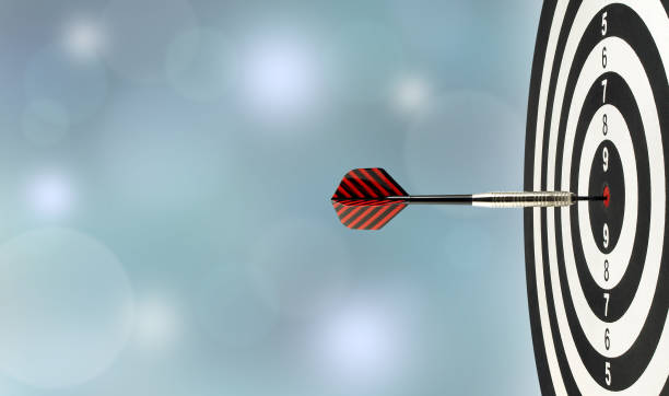 closeup silver metal dart arrow hitting red bulls eye target center of wooden dartboard with blurred blue lights bokeh copy space background perfection goal success, symbol of aim and achievement dartboard stock pictures, royalty-free photos & images