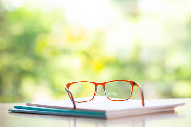 istock Orange eyeglasses with three white notebook on wooden table, Bokeh garden background, Close up & Macro shot, Selective focus, Stationery concept 1133510634