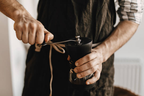 aeropress のための黒い流行のエプロンの粉砕のコーヒーの専門のバリスタ、代わりとなる醸造方法。コーヒー豆と手動グラインダーを保持する手。代替コーヒーのためのアイテム - grind ストックフォトと画像