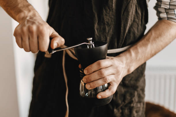 istock Hands holding manual grinder  with coffee beans. Items for an alternative coffee. Professional barista in black stylish apron grinding coffee for aeropress, alternative brewing method 1133511593