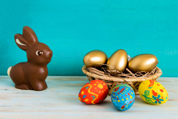 istock Happy Easter concept with color ang gold eggs in basket next to chocolate Easter bunny on blue wooden background 1133514091