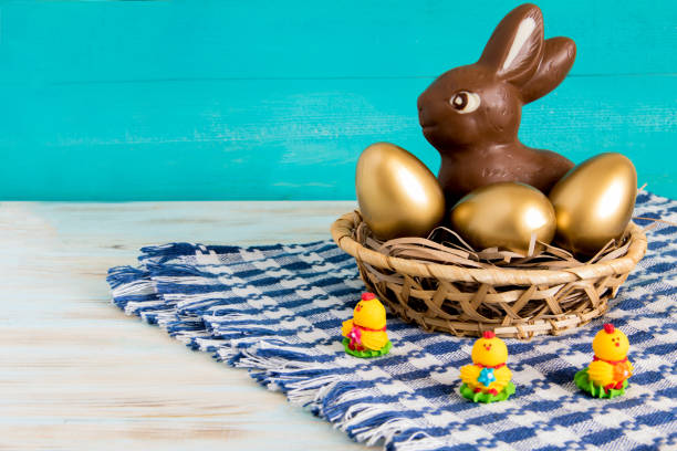 lapin de pâques au chocolat dans le panier avec des oeufs de pâques or et jaune bébé poulet sur fond en bois bleu - figurine easter egg easter holiday photos et images de collection