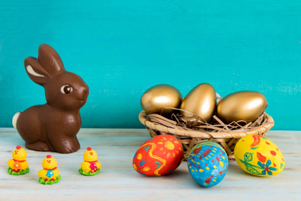 istock Happy Easter concept with color ang gold aster eggs in basket next to chocolate Easter bunny and baby chicken on blue wooden background 1133514133
