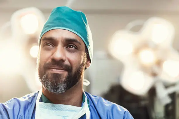 Bearded male surgeon looking away. Doctor is working in illuminated operating room. He is wearing scrubs.