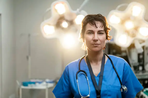 Portrait of confident female surgeon. Healthcare worker is against illuminated lights in hospital. She is having short hair.