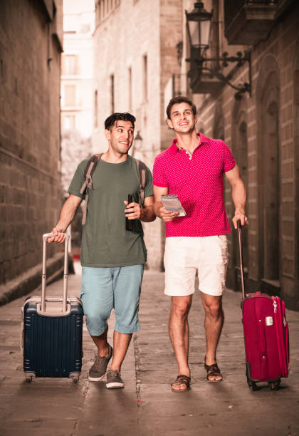 Two cheerful positive smiling friends are walking with beer and watching to historical sights in Barcelona.