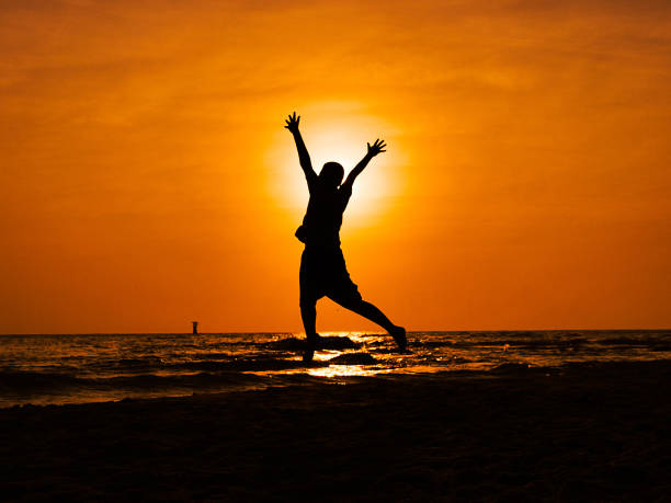 istock Silhouette boy jumping and raising hands on the beach in sun rise. 1133518192