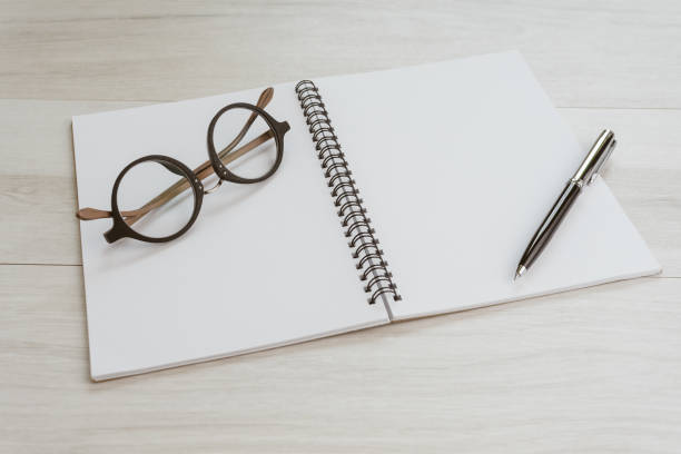 Blank empty white page note book opening with pen and eyeglasses on gray wooden table using as thinking, writing and creativity.