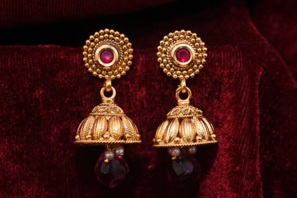 paar aus fancy goldenen designer-ohrringen, die makro-bild auf rotem hintergrund verdecken - gold earrings stock-fotos und bilder