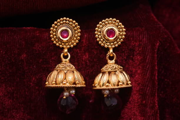 paire de fantaisie or boucles d'oreilles créateur gros plan macro image sur fond rouge - gold earrings photos et images de collection