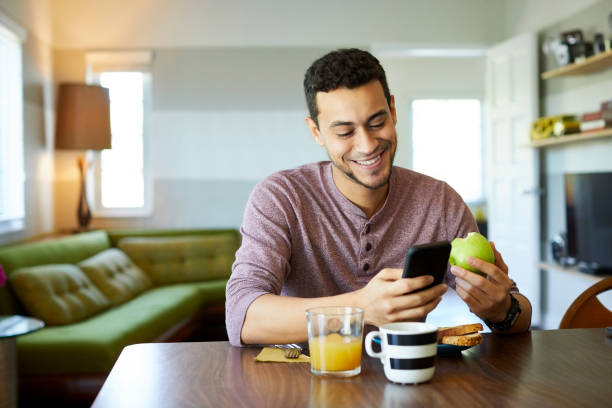 homem de sorriso que usa o telefone móvel ao prender a maçã - granny smith apple apple food fruit - fotografias e filmes do acervo