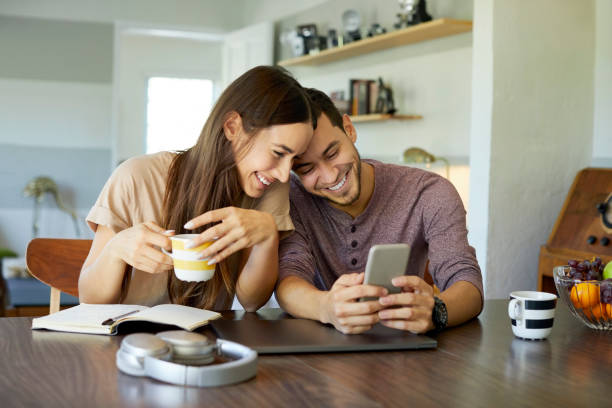 pareja alegre utilizando el teléfono móvil en el comedor - pareja joven fotos fotografías e imágenes de stock