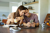 Cheerful couple using mobile phone in dining room