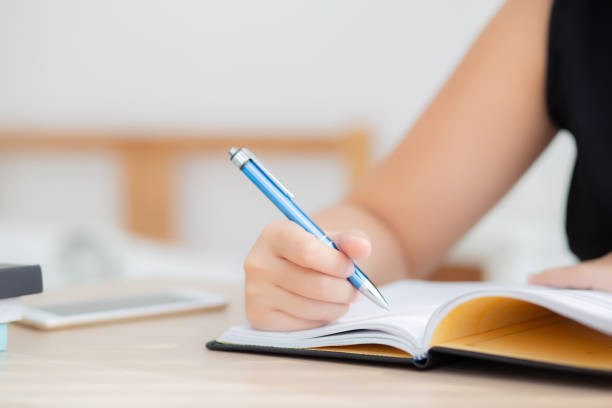 istock Closeup hand asian woman sitting study and learning writing notebook and diary on table in living room at home, girl homework, business writer woman working on table, education concept. 1133527567