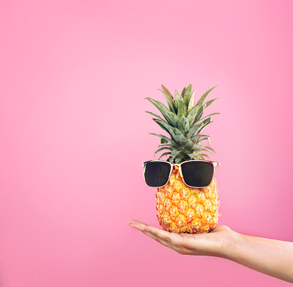 Cropped shot of a woman holding a pineapple with sunglasses on