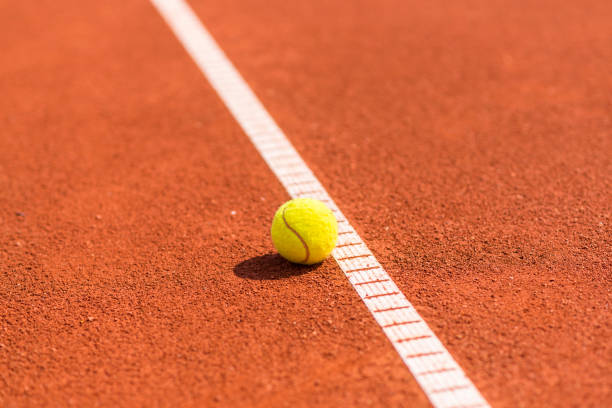 Yellow tennis ball on sand tennis court Yellow tennis ball on a sand orange tennis court clay court stock pictures, royalty-free photos & images