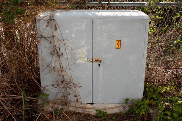 istock Grey electrical high voltage outdoor box closed with rusted latch located at abandoned industrial complex surrounded with dry plants and metal fence 1133535489