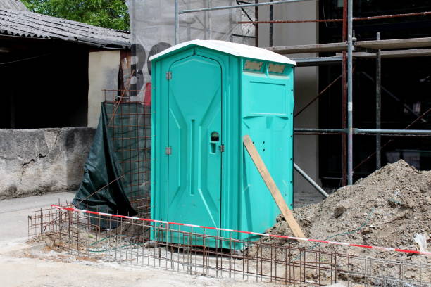 istock Light green portable ecological toilet left on construction site surrounded with sand and other construction material with old house in background 1133535498