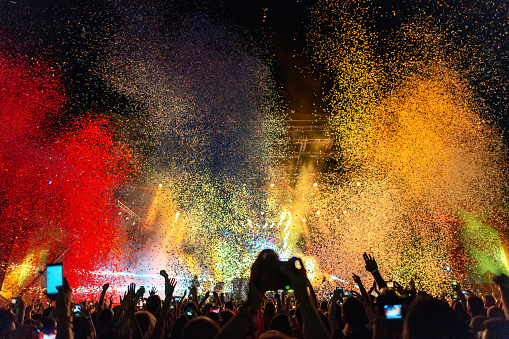 Crowd of people having fun while watching colorful confetti fireworks at music festival.