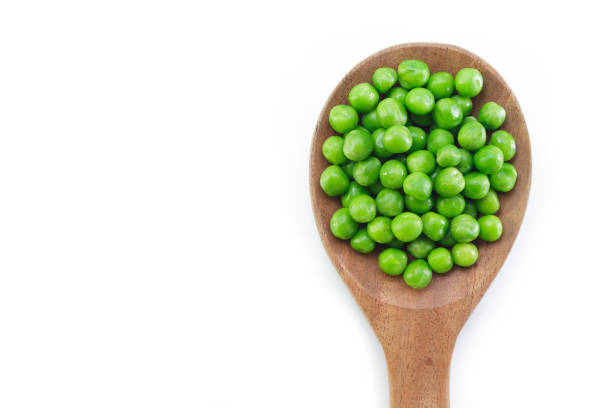 istock green peas on wooden spoon on white background. 1133540413