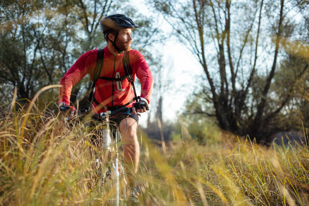 jeune homme satisfait chevauchant le vélo de montagne à travers la prairie par l'herbe haute - cycling cyclist bicycle men photos et images de collection